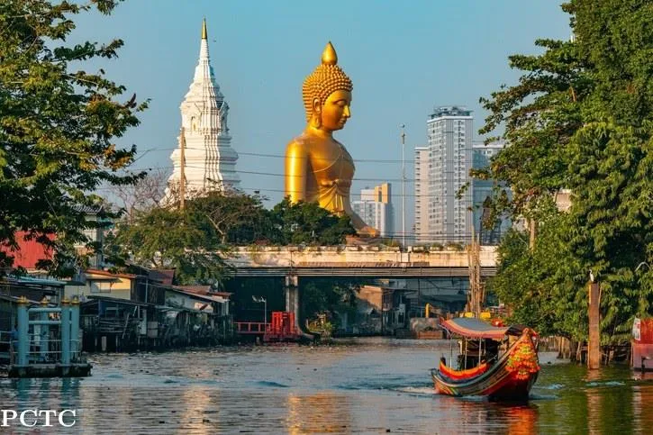 A giant golden Buddha beside a white temple spire over a Bangkok canal